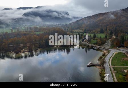 Drone vue aérienne du lac Bohinj reflétant l'église de St jean baptiste sous les nuages bas, entouré d'arbres d'automne colorés dans les alpes juliennes, Sloven Banque D'Images