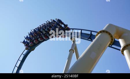 Les gens traversent une inversion sur les montagnes russes inversées intenses 'Ozlris' du fabricant 'B&M' dans le parc à thème 'Astérix' sous un SK bleu Banque D'Images