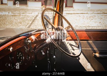 Lisbonne, Portugal - 29 septembre 2024 : gros plan et focus sélectif sur l'intérieur vintage de luxe Rolls-Royce Phantom III 1937. Volant et tableau de bord en bois, cuir et chrome éclairés par la lumière du soleil. Banque D'Images