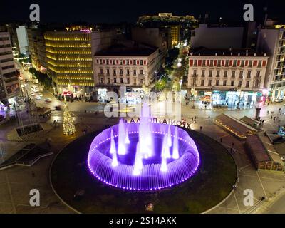 Vue nocturne de la place Omonoia avec fontaine colorée, arbre de Noël et rues animées. Acropole dans le dos. Athènes Banque D'Images