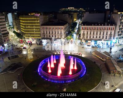 Vue nocturne de la place Omonoia avec fontaine colorée, arbre de Noël et rues animées. Acropole dans le dos. Athènes Banque D'Images