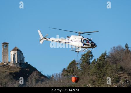 Hélicoptère en vol pour une opération de lutte contre les incendies près d'Illegio (Frioul-Vénétie Julienne). Transport par eau avec panier, fond avec église paroissiale. Banque D'Images