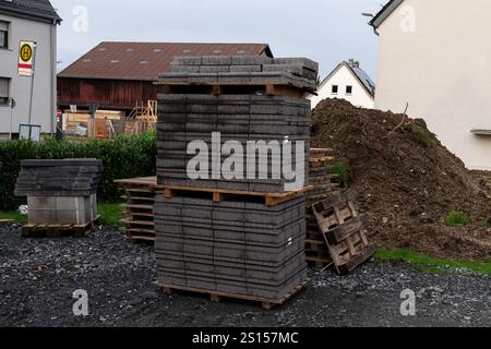 Blocs de construction gris empilés sur des palettes en bois près d'un site en développement avec un terrain de gravier. Un fond de monticules de terre et de bâtiments définit la scène Banque D'Images