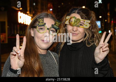 Broad Street, Birmingham 31 décembre 2024 - deux femmes posent pour une photo avec des lunettes NYE 2025 mais doivent s'accrocher à eux en raison du vent fort. - Les fêtards sont partis dans le centre-ville de Birmingham tôt la Saint-Sylvestre. Crédit : British News and Media/Alamy Live News Banque D'Images