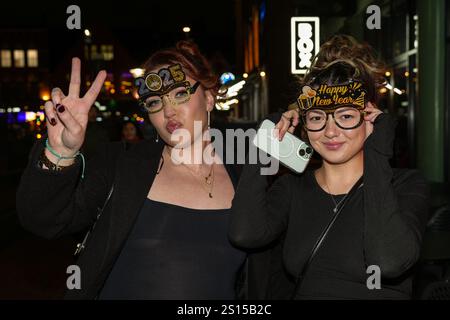 Broad Street, Birmingham 31 décembre 2024 - deux femmes posent pour une photo avec des lunettes NYE 2025 mais doivent s'accrocher à eux en raison du vent fort. - Les fêtards sont partis dans le centre-ville de Birmingham tôt la Saint-Sylvestre. Crédit : British News and Media/Alamy Live News Banque D'Images