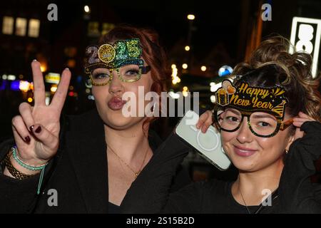 Broad Street, Birmingham 31 décembre 2024 - deux femmes posent pour une photo avec des lunettes NYE 2025 mais doivent s'accrocher à eux en raison du vent fort. - Les fêtards sont partis dans le centre-ville de Birmingham tôt la Saint-Sylvestre. Crédit : British News and Media/Alamy Live News Banque D'Images