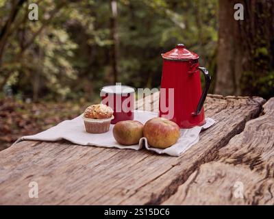 Snack dans les bois. Muffin, pommes, tasse rouge et cafetière sur la table de pique-nique. Déjeuner en plein air en automne hiver Banque D'Images