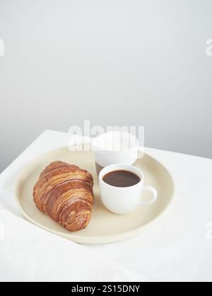 Petit déjeuner continental simple sur la table croissant, tasse à café et pichet à lait Banque D'Images
