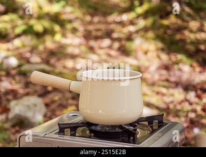 Cuisiner à l'extérieur. Casserole émaillée vintage sur cuisinière à gaz portable sur table en bois dans la forêt Banque D'Images