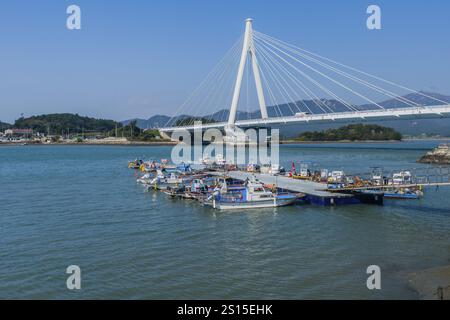 Pont suspendu sur l'eau avec plusieurs petits bateaux amarrés à proximité, sur fond de montagnes, situé à Wando, Corée du Sud, Asie Banque D'Images