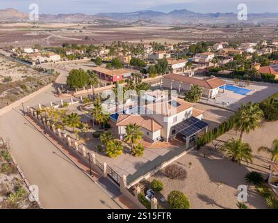 Vue aérienne d'une villa spacieuse avec panneaux solaires, piscine privée, jardin luxuriant et paysage pittoresque sous un ciel dégagé. Banque D'Images