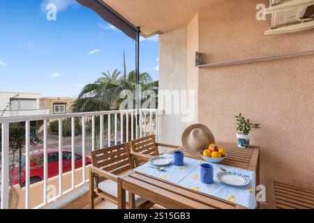 Charmant balcon situé sur la Costa Blanca, en Espagne, doté d''un service à manger en bois, de fruits frais et d''une vue relaxante sur les palmiers. Banque D'Images