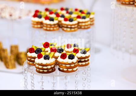 La table des desserts magnifiquement agencée présente des biscuits superposés recouverts de baies fraîches à la crème fouettée, créant une atmosphère accueillante pour les événements festifs des invités. Banque D'Images