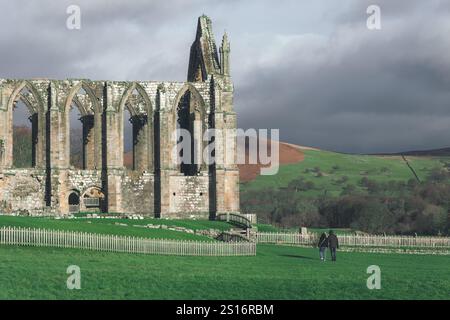 Deux personnes marchant vers les ruines du prieuré de Bolton à Bolton Abbey près de Skipton sur le bord du Yorkshire Dales National Park en Angleterre. Banque D'Images