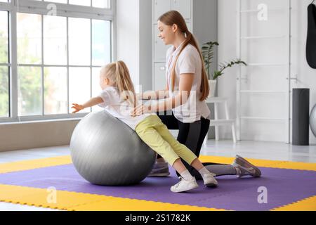 Mignonne petite fille de formation avec fitball et entraîneur dans le gymnase Banque D'Images