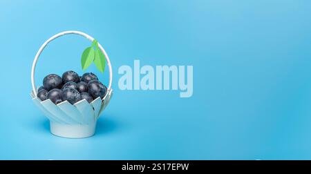 Bleuets crus frais dans un panier en papier blanc fait maison avec des feuilles vertes sur un fond bleu. Copier l'espace Banque D'Images
