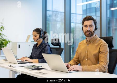 Portrait de l'employé de support à la clientèle de service à la clientèle, homme avec casque souriant et regardant la caméra, équipe travaillant à l'intérieur de l'immeuble de bureaux avec ordinateur portable. Banque D'Images