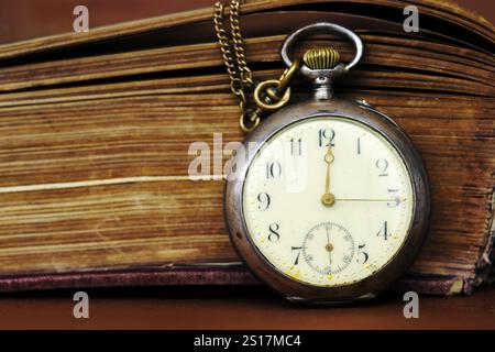 Une ancienne montre de poche se penche contre un vieux livre avec pages jaunrées Banque D'Images