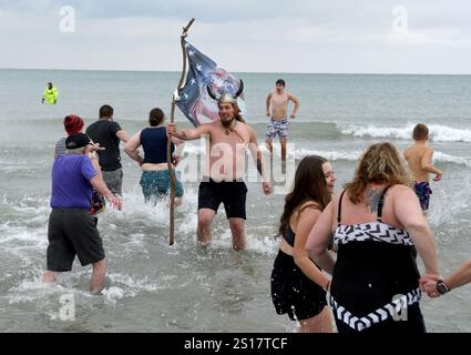 Racine, Wisconsin, États-Unis. 1er janvier 2025. Christian Jackson tend son drapeau américain avec des mains tenant la Terre à son ami Roy Bohn alors que les nageurs se dirigent vers le lac Michigan pour le 35e plongeon polaire annuel du jour de l'an de Splash and Dash à midi, le 1er janvier 2025. Bohn a dit que la Terre est «la planète que nous ruinons». La température de l'eau était de 39,6 degrés, la température de l'air était de 29, avec un refroidissement éolien de 9 degrés. Chacun des trois derniers plongeons a permis d’en récolter plus de ,000 pour la banque alimentaire du comté de racine et HALO (Homeless assistance leadership Organization). La Fondation Kiwanis Banque D'Images