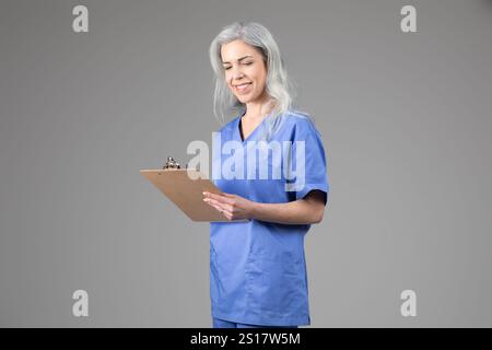 Professionnel de la santé souriant avec presse-papiers dans des gommages bleus Banque D'Images