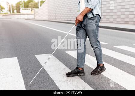 Jeune homme noir malvoyants méconnaissable avec canne à pied de l'autre côté de la rue de la ville, en gros plan Banque D'Images