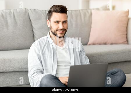 Concept de travail à distance. Jeune indépendant à succès travaillant sur ordinateur portable, assis sur le sol, travaillant à distance depuis la maison Banque D'Images