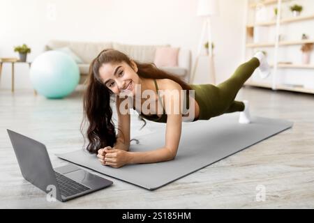 Femme indienne forte debout dans le coude de planche devant l'ordinateur portable, de l'activité sur le tutoriel de sport en ligne à la maison Banque D'Images