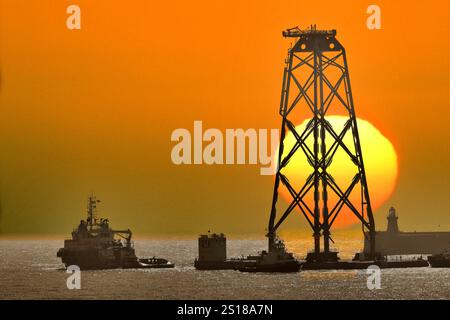 Grande base d'éoliennes quittant la rivière Tyne pour un parc éolien dans la mer du Nord contre un soleil levant massif et un ciel d'aube orange Banque D'Images