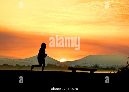 Coureur masculin matinal brumeux tôt avec haut à capuche contre le ciel rouge et le soleil se levant entre les montagnes Banque D'Images