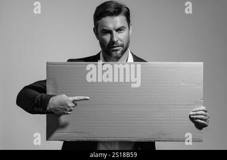 L'homme en costume tient le signe avec l'espace de copie. Affiche prête pour le produit de l'espace de copie. Signez le texte de votre espace de copie. Homme montrant un tableau blanc sur le backgrou de studio Banque D'Images