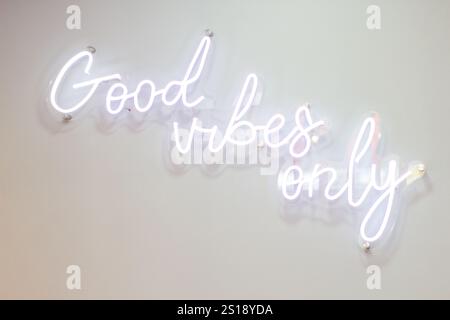 Enseigne au néon indiquant « Only Good Vibes » en blanc brillant, sur un fond mural blanc Banque D'Images