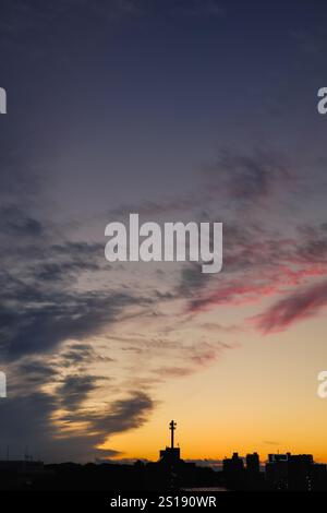 Les teintes des nuages sinueux passent du bleu ombré au rouge orange sang alors qu'elles s'évanouissent d'un amas de nuages s'élevant au-dessus de l'horizon silhouetté. Banque D'Images