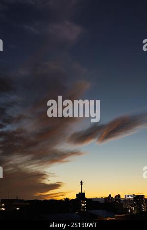 De légères stries de ficelle orange à travers des nuages tordus empilés verticalement flottant dans le ciel crépusculaire, ressemblant à des braises faiblement incandescentes dans un feu de camp. Banque D'Images