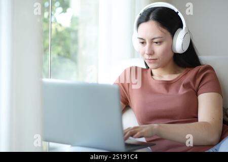 Femme asiatique portant un casque à l'aide d'un ordinateur portable assis sur un canapé à la maison Banque D'Images