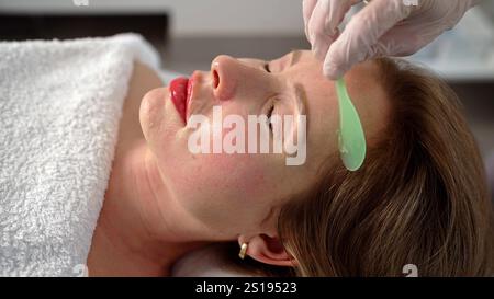 Application de gel sur le visage dans un salon de beauté. Une femme médecin cosmétologue applique un gel sur le visage d'une jeune femme. Banque D'Images