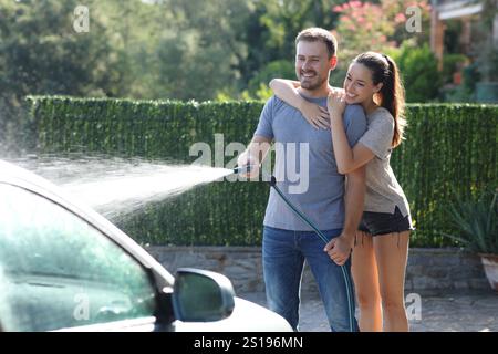 Couple heureux lavant l'arrosage de voiture avec tuyau de tuyau à la maison Banque D'Images