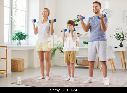 Famille de père, mère et enfant garçon faisant des exercices sportifs avec des haltères à la maison Banque D'Images