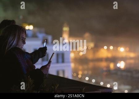 Trani, Italie. 1er janvier 2025. Les gens enregistrent le concert en utilisant leur téléphone portable depuis une terrasse alors que le chanteur Tony Hadley se produit avec son groupe, Spandau Ballet pour le concert de la Saint-Sylvestre dans la ville côtière de Trani. Crédit : SOPA images Limited/Alamy Live News Banque D'Images