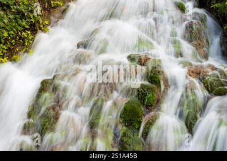 Une cascade époustouflante descend en cascade sur un terrain montagneux accidenté, entouré d'un feuillage vert vibrant. Banque D'Images