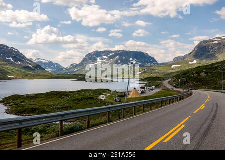 Une route sinueuse traverse un magnifique paysage norvégien, avec une végétation luxuriante, des lacs clairs et des montagnes majestueuses. Ciel partiellement nuageux Banque D'Images