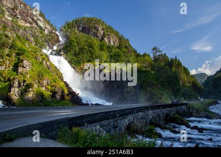Latefossen, une superbe cascade coule sur des falaises rocheuses le long d'une route sinueuse. Une végétation luxuriante entoure la région, créant une atmosphère paisible Banque D'Images
