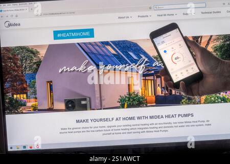 Main tenant l'application de contrôle de pompe à chaleur sur un smartphone en face du site Web de pompes à chaleur Midea. Banque D'Images