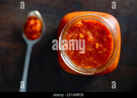 Pot en verre avec des légumes hachés frais en conserve, lecho sur fond noir. Conserves maison. Sauce tomate rouge et poivrons maison naturelle avec sp Banque D'Images