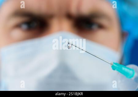 Goutte de médicament sur l'extrémité de l'aiguille d'injection médicale. Docteur en masque médical avec seringue se préparant à l'injection. Mise au point de vaccins. Goutte de liquide Banque D'Images