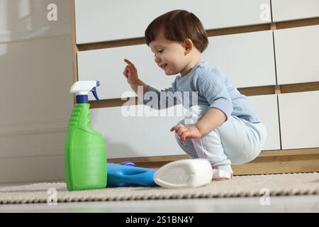 Petit garçon jouant avec des bouteilles de détergents près de l'armoire à la maison. Enfant en danger Banque D'Images