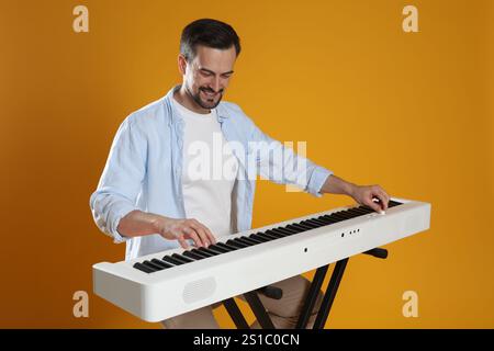 Homme barbu jouant synthétiseur sur fond orange Banque D'Images