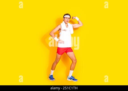 Jeune homme en tenue de sport fléchissant les biceps sur fond jaune vif, incarnant l'énergie et la santé Banque D'Images