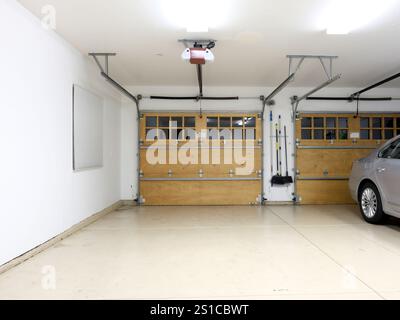 Bien éclairé propre, soigné et clairsemé garage de deux voitures dans une maison résidentielle moderne ; un côté vide sans voiture et l'autre avec une voiture garée. Banque D'Images