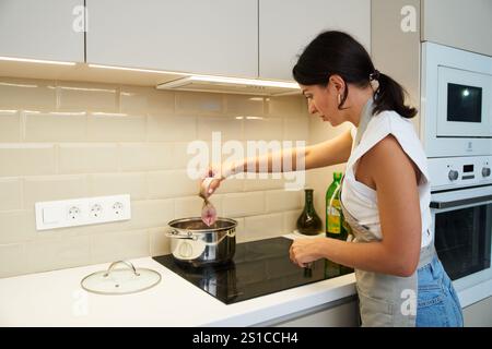 Femme cuisinant dans une cuisine moderne tout en préparant de la viande dans une casserole sur le poêle Banque D'Images