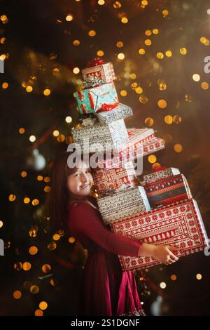 Fille tenant une pile de cadeaux debout devant des lumières scintillantes Banque D'Images